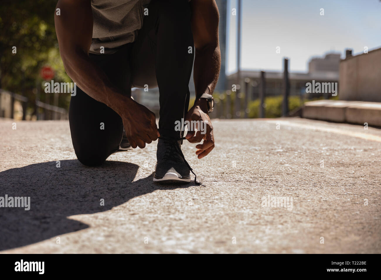 Man tying his shoe lace while crouching at pavement Stock Photo