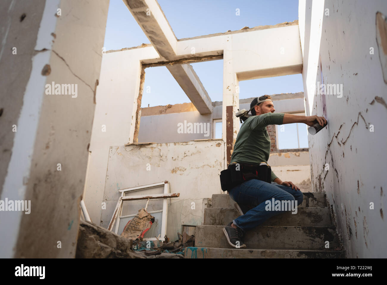 Graffiti artist spray painting on weathered wall while sitting on ...