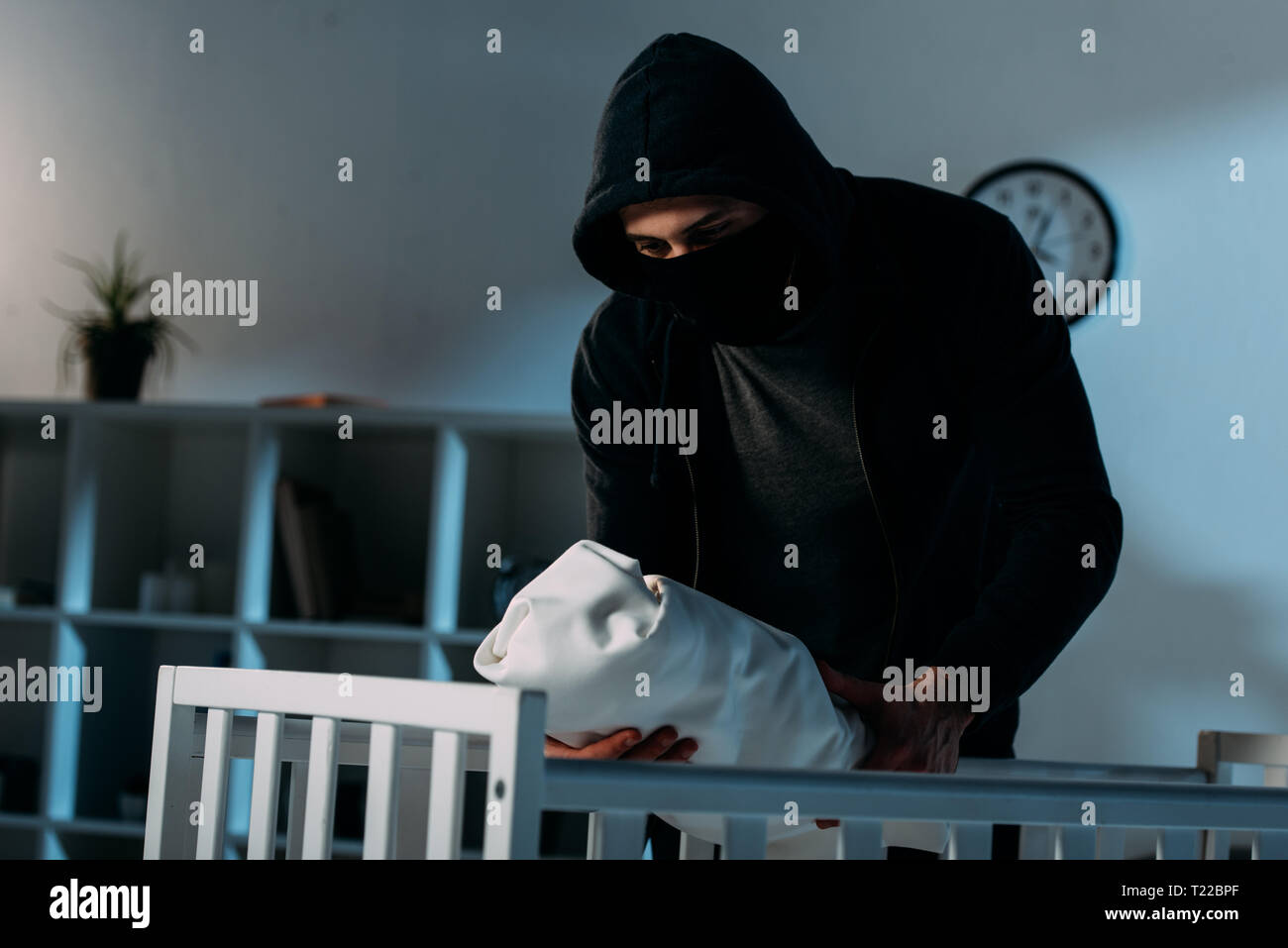Kidnapper in mask and hoodie standing near crib and holding infant ...