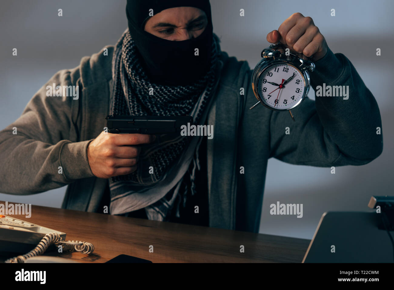 Aggressive terrorist holding gun and alarm clock at table Stock Photo