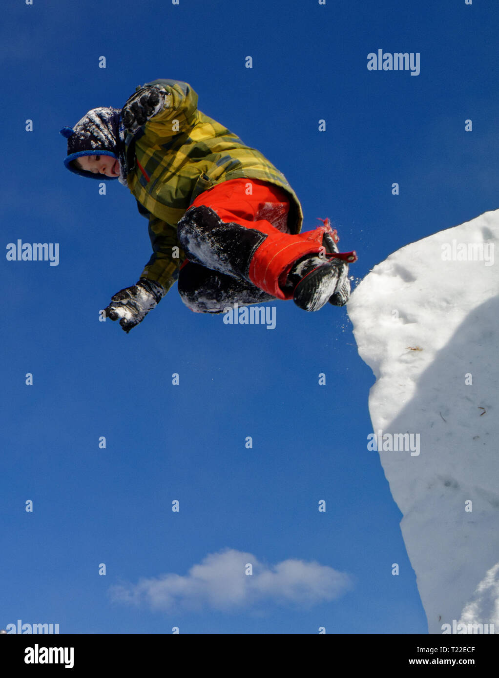 A young boy (6 yrs old) jumping from the top of a snow cliff Stock Photo