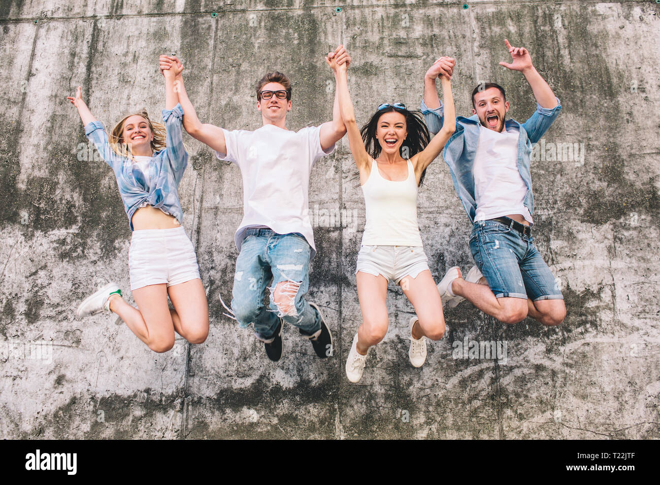 Awesome and nice people are jumping up in the air. They are holding their hands up in the air too. Company is on the grey background. They are positiv Stock Photo