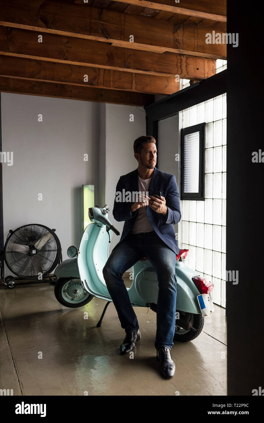Man with motor scooter in a loft using cell phone Stock Photo