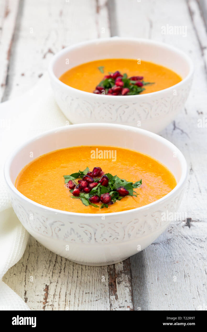 Bowls of carrot ginger coconut soup with topping of parsley and pomegranate seed Stock Photo