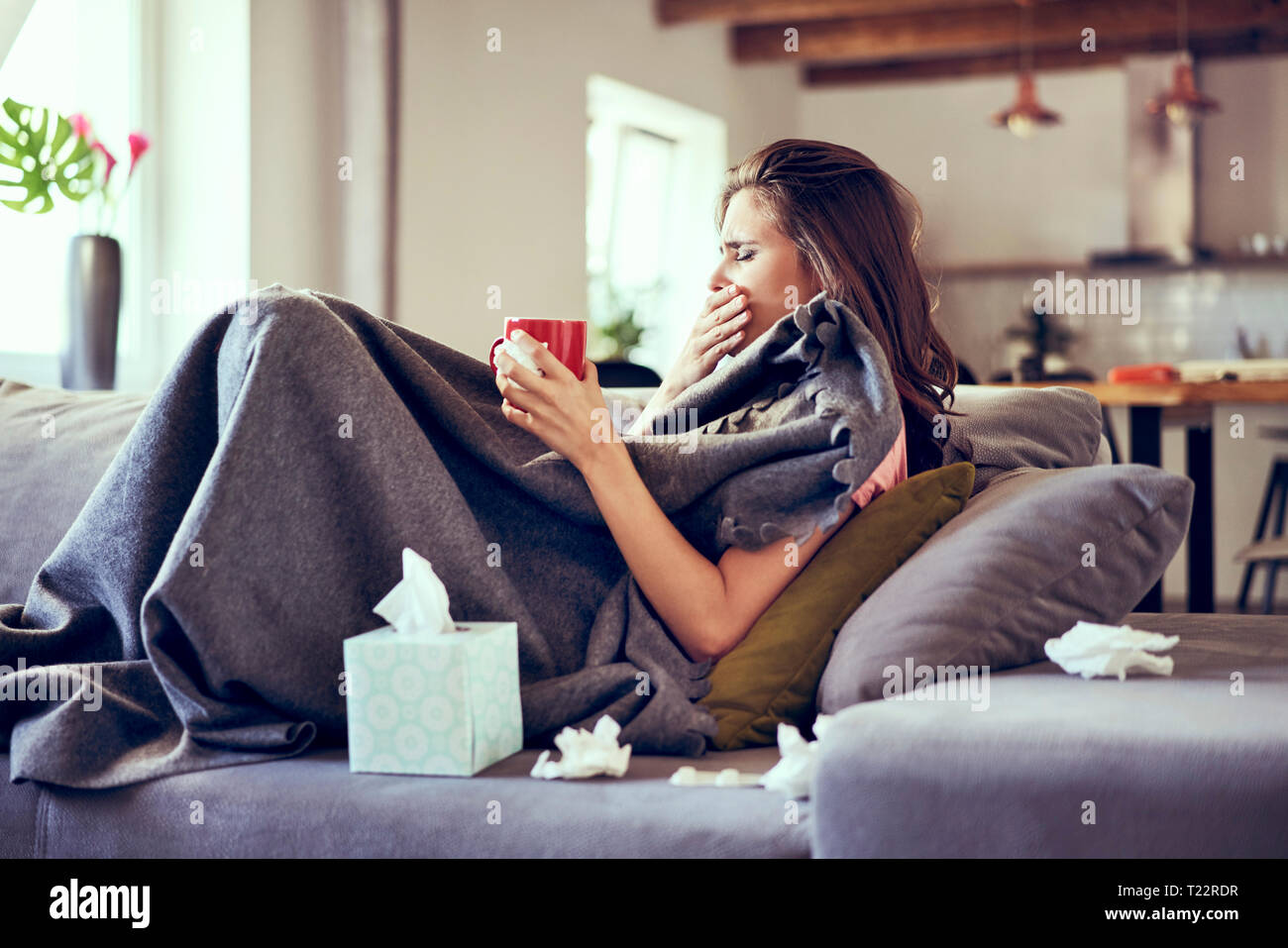 Portrait of woman lying sick on sofa coughing and trying to drink hot tea Stock Photo