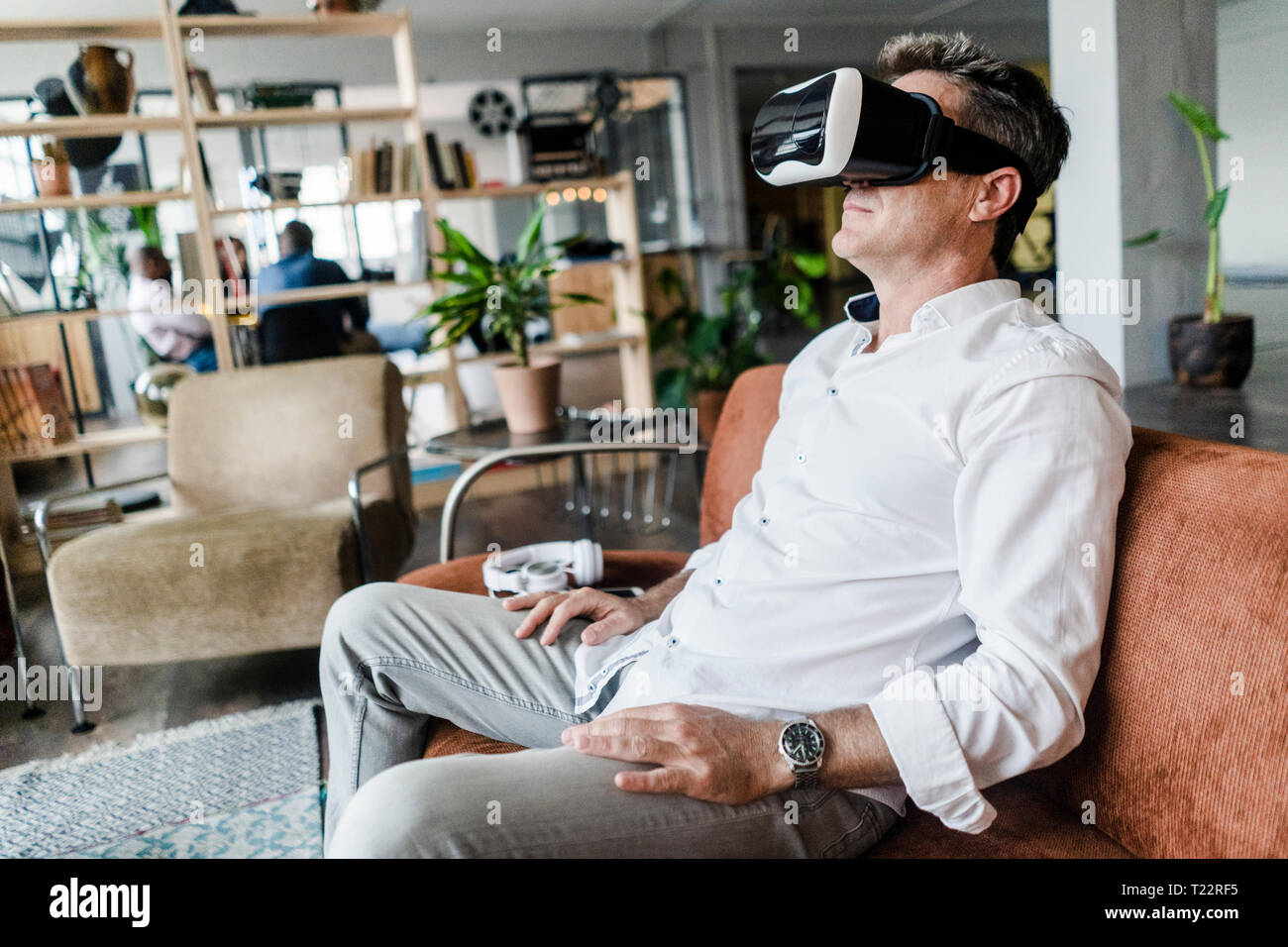 Mature man wearing VR glasses sitting on couch in a loft Stock Photo