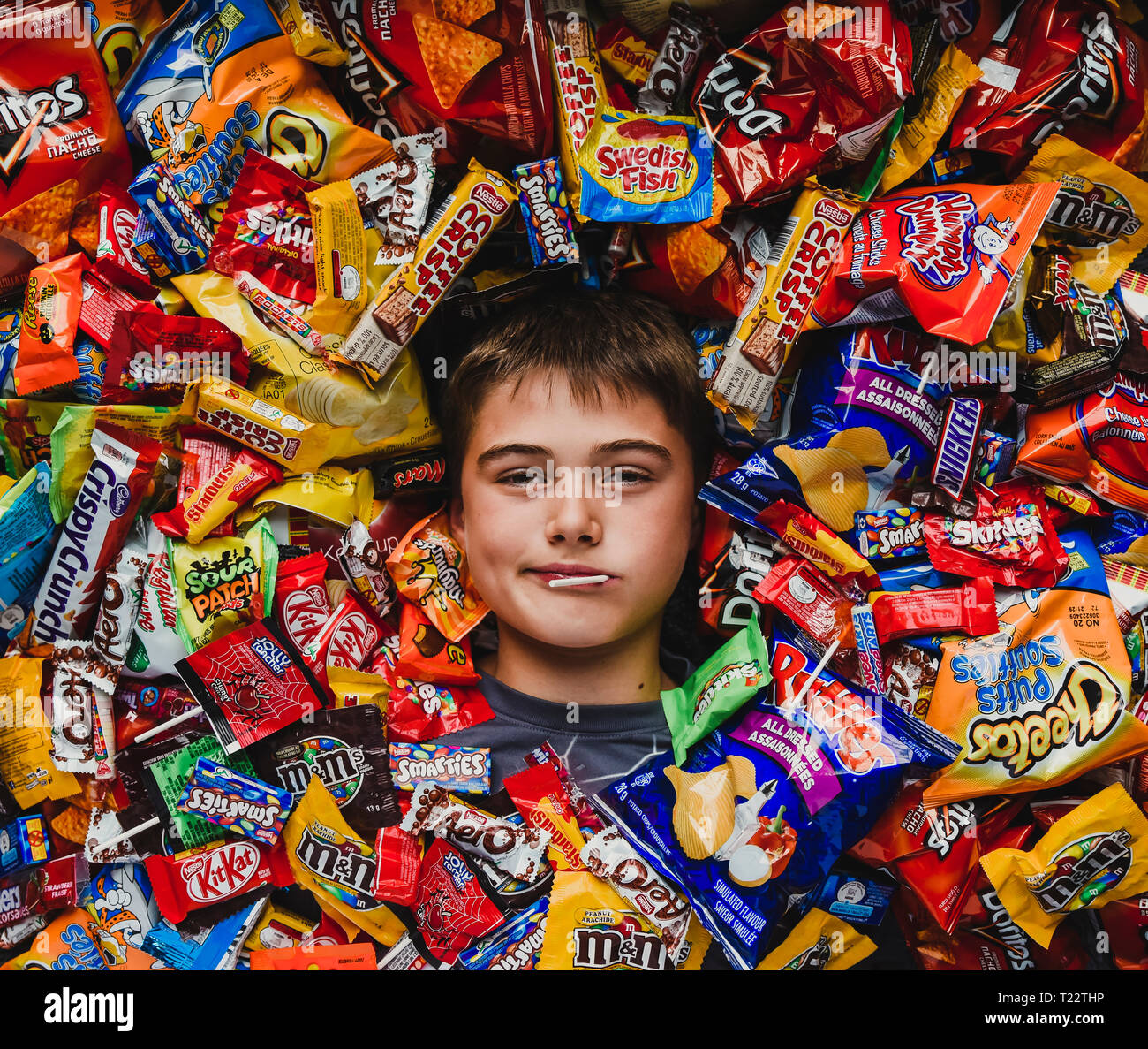Adolescent boy laying down surrounded by junk food eating lollipop Stock Photo