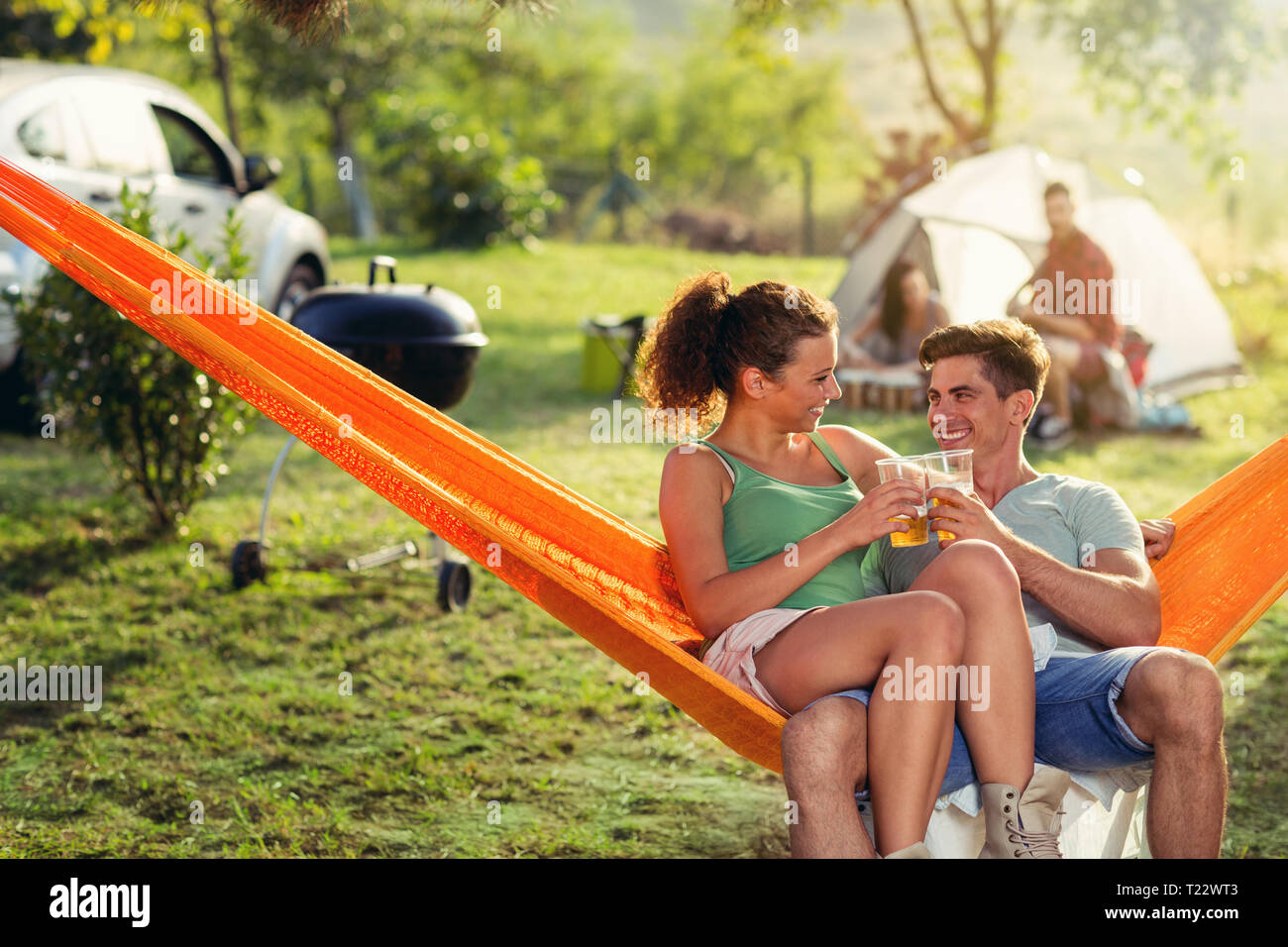 Love young couple sitting in hammock chair and toasted with beer , vacation on countryside Stock Photo