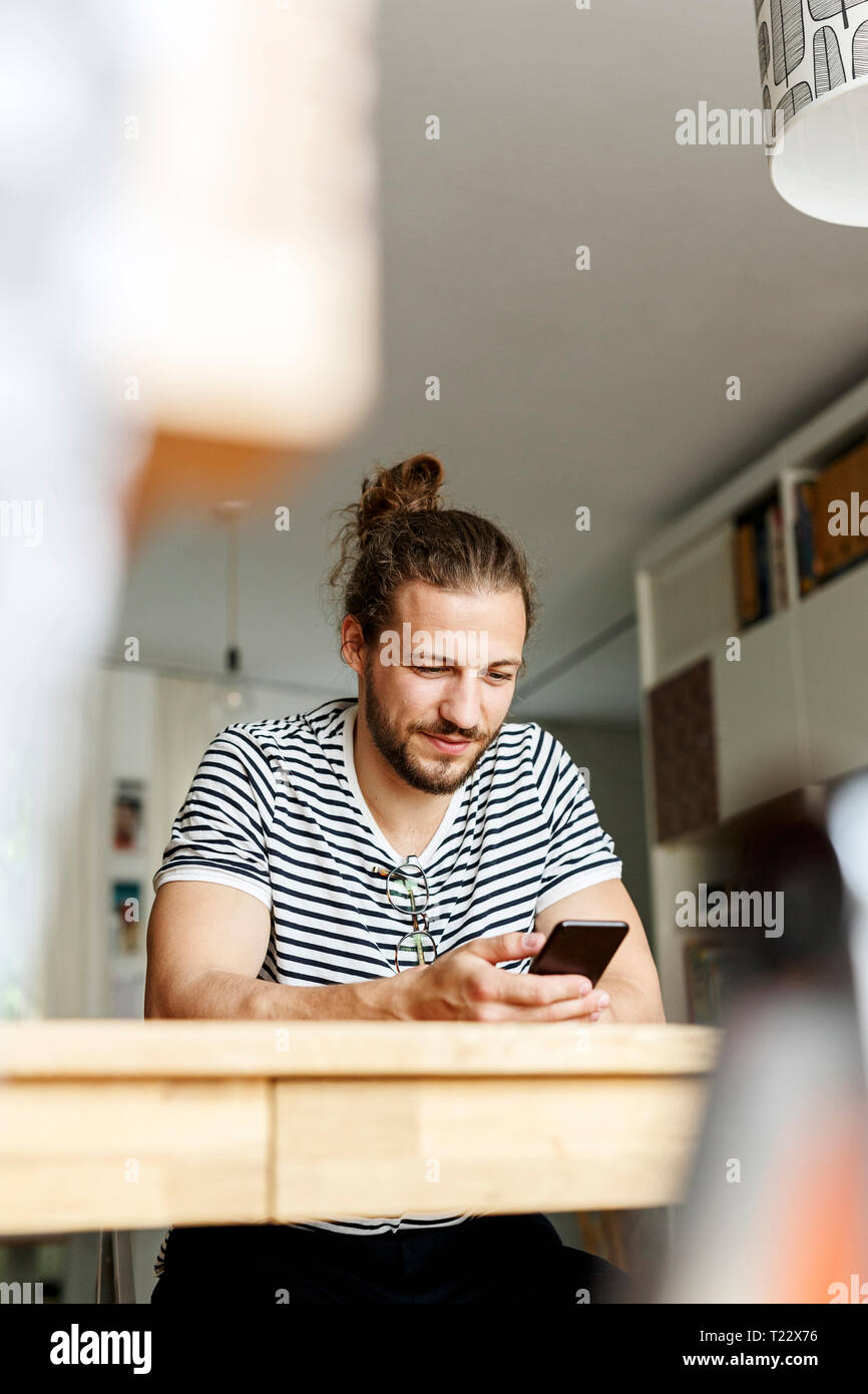 Young man with a bun sitting at home, using smartphone Stock Photo