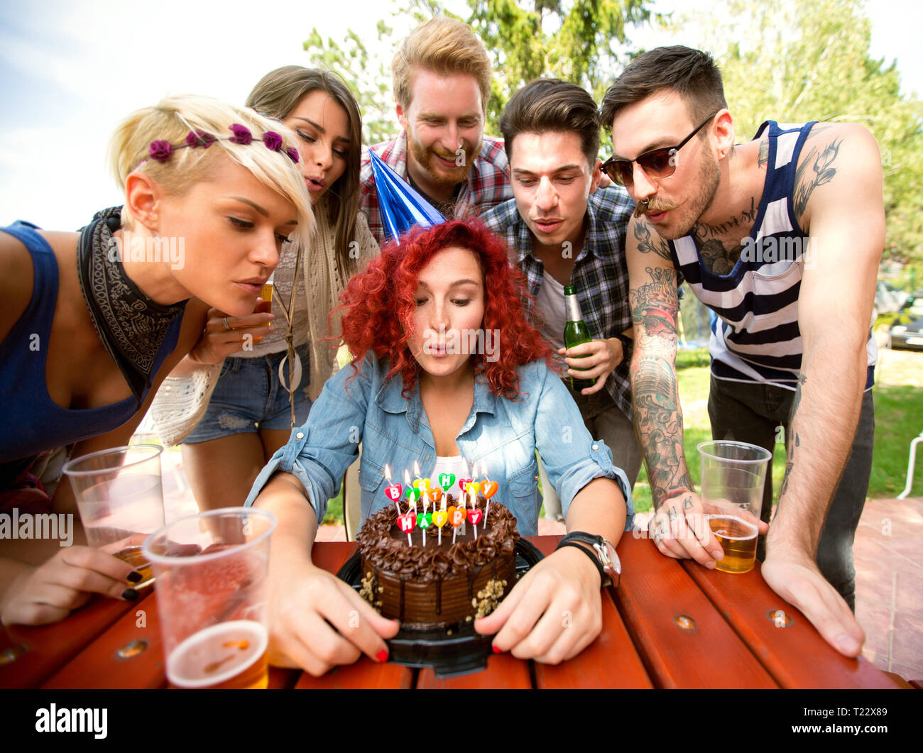 Delighted curly ginger birthday girl blow colorful candles on  birthday cake in nature Stock Photo