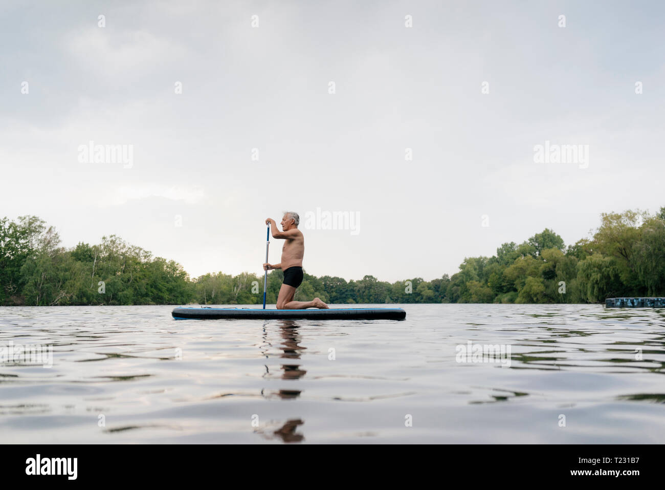 Senior man kneeling on SUP board Stock Photo