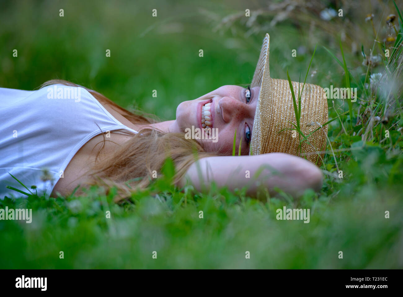 Portrait of laughing teenage girl wearing straw hat lying on a meadow ...