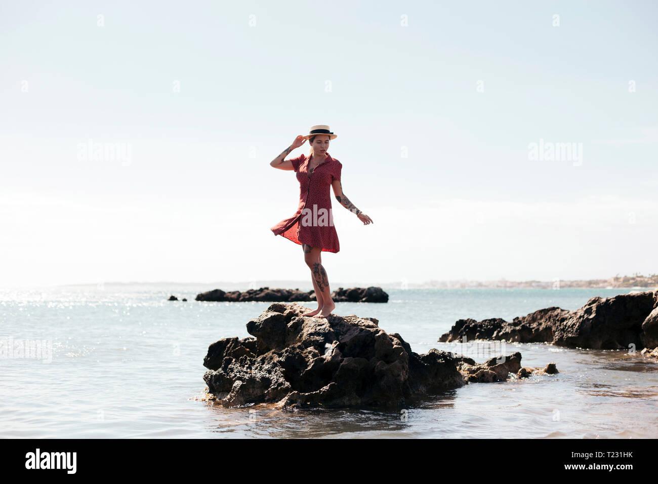 Spain, Mallorca, tattooed young woman standing on a rock looking at ...