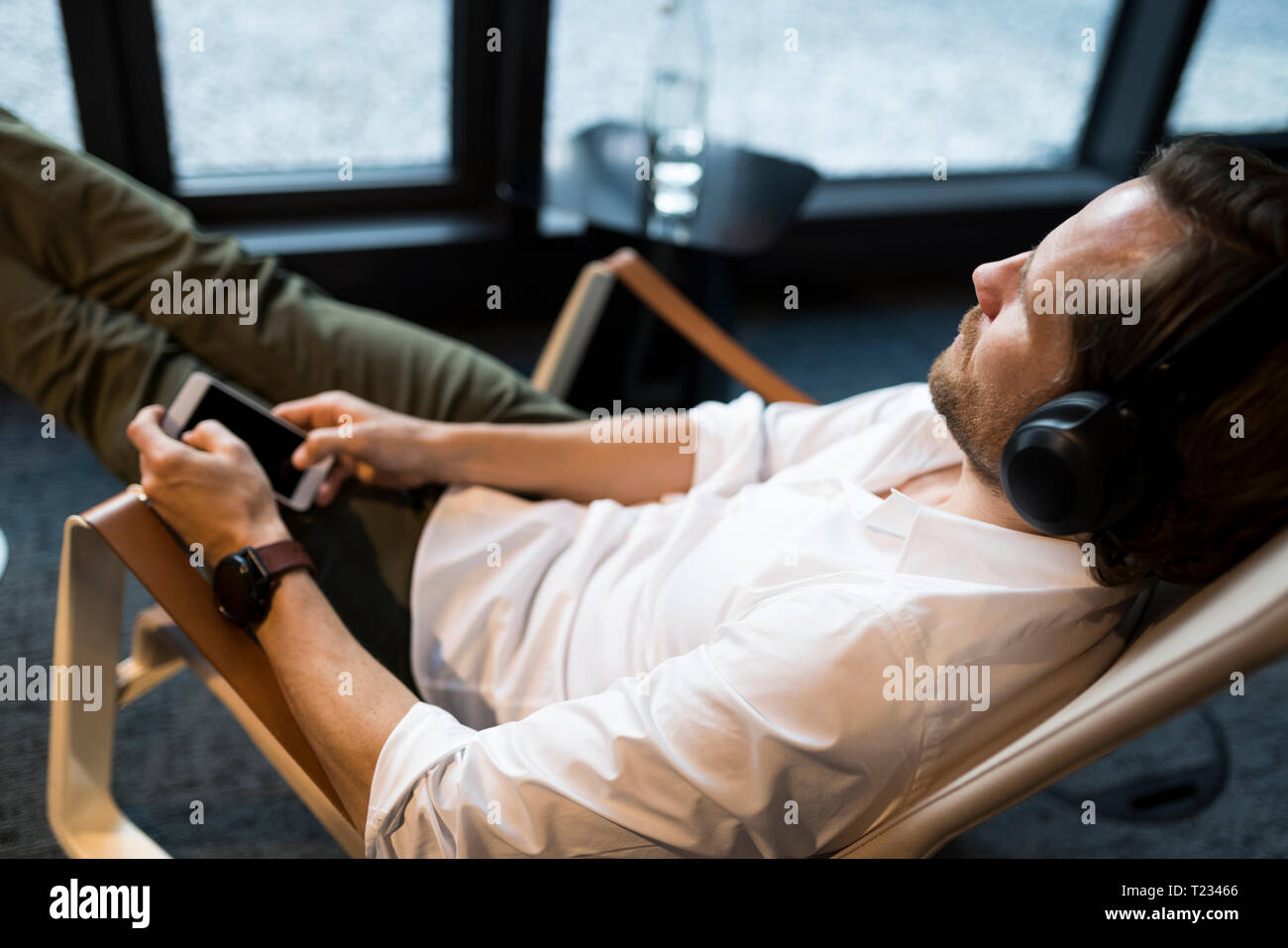 Casual businessman relaxing in lounge area of a coworking space, listening music Stock Photo