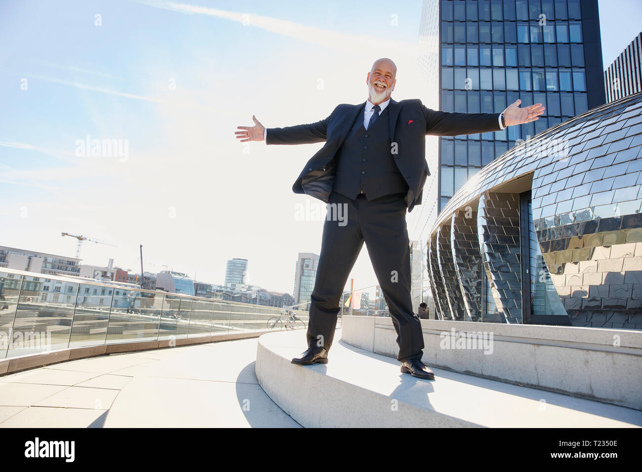 Elegant businessman standing with arms out in the city, laughing happily Stock Photo
