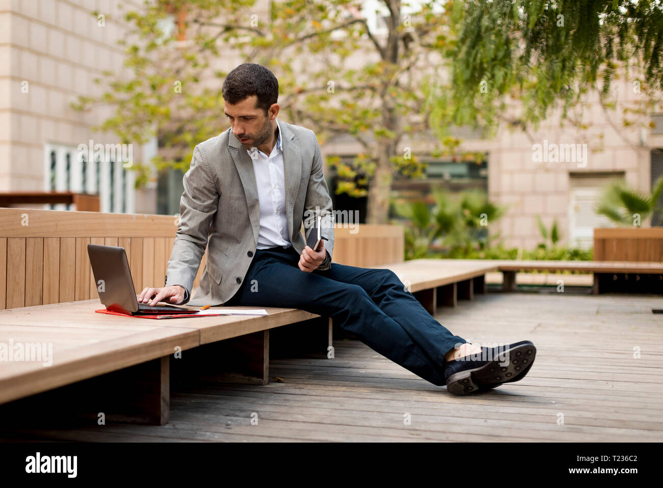 Businessman sitting on a bench using laptop Stock Photo