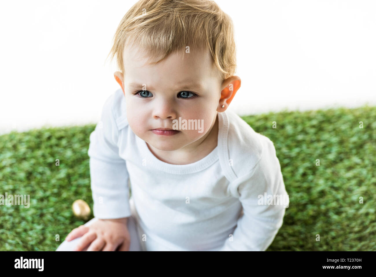 Adorable Kid With Blonde Hair Sitting On Green Grass Isolated On