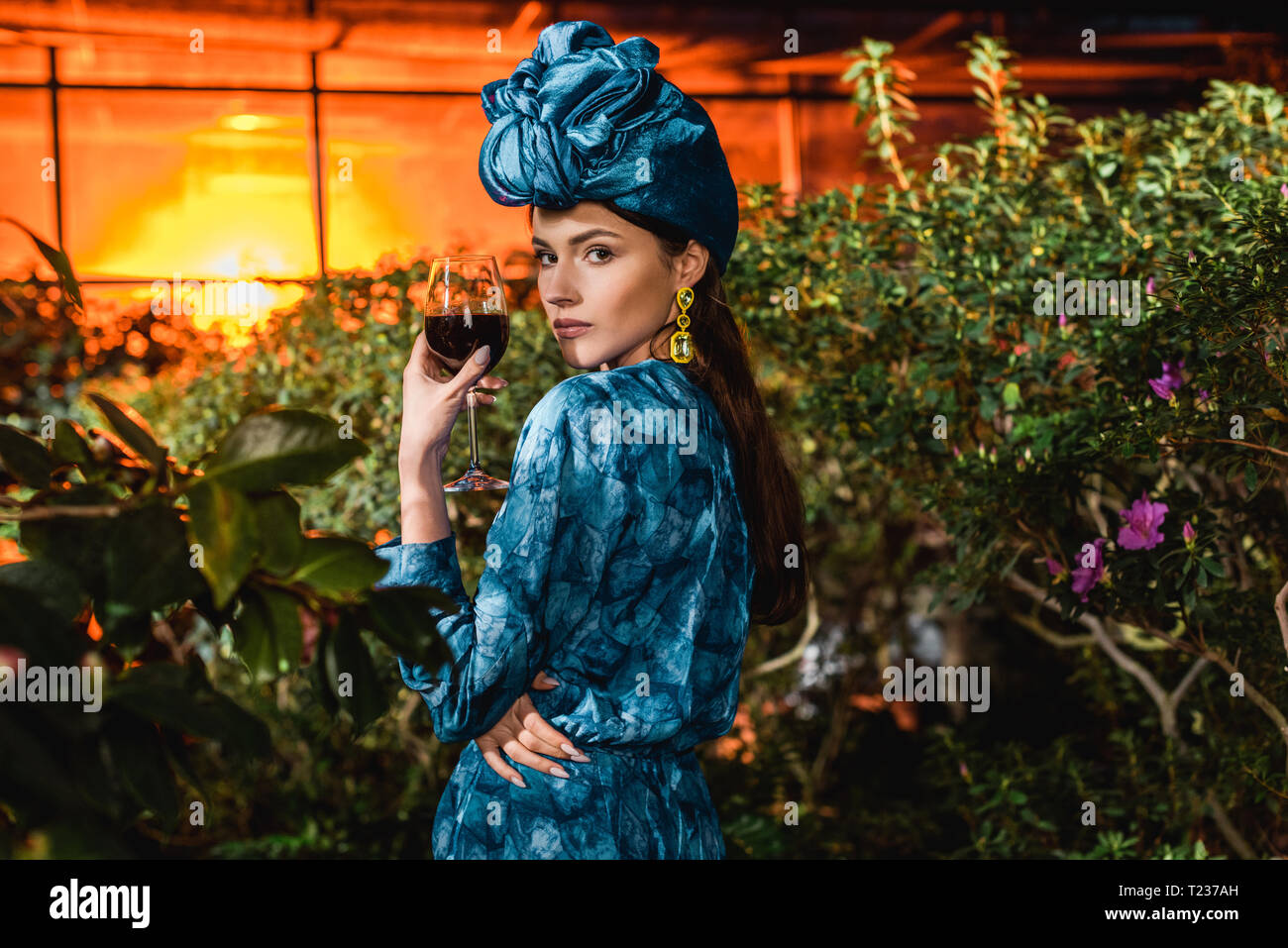 Attractive woman in blue turban holding glass of red wine in orangery Stock Photo