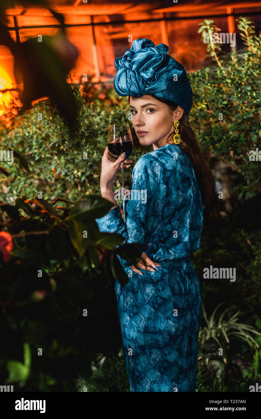 Attractive woman in blue turban holding glass of red wine in orangery Stock Photo