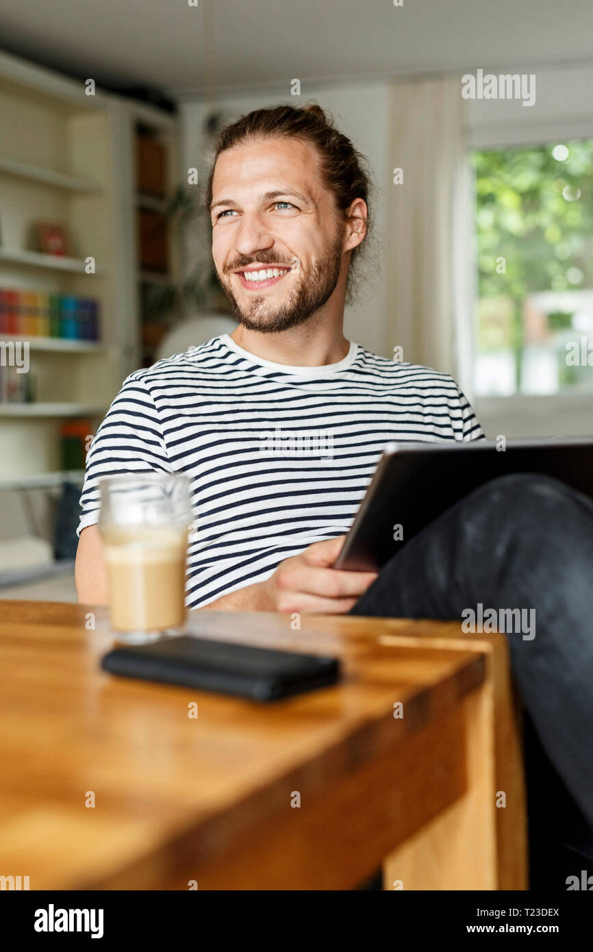 Young man with a bun sitting at home, using digital tablet Stock Photo