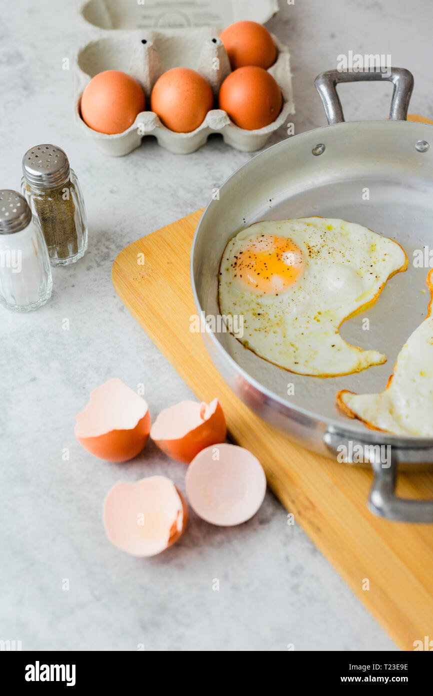 Eggs in a box, fried eggs in pan and eggshells Stock Photo
