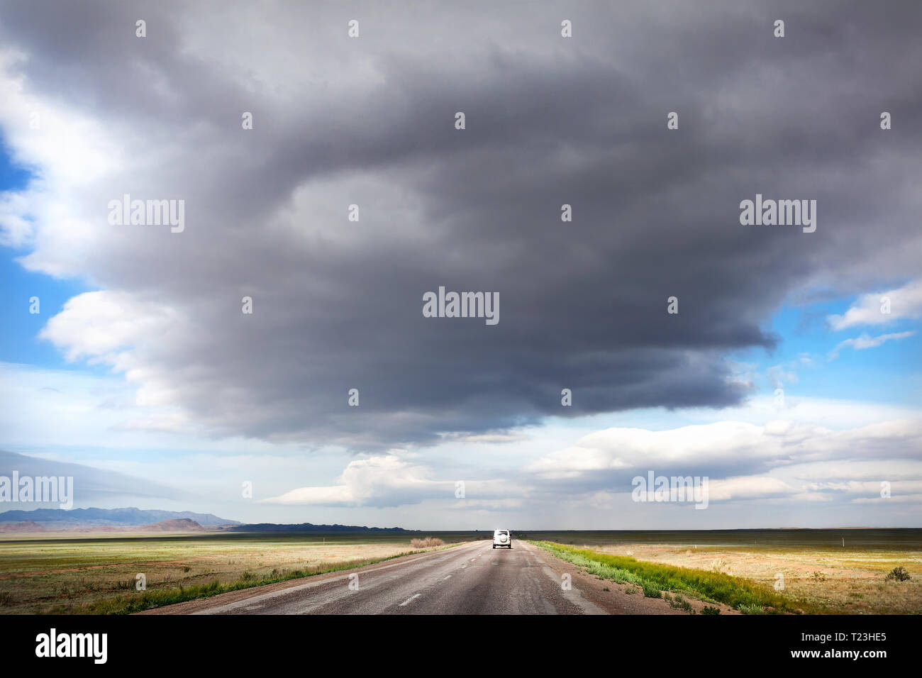 Highway road and lonely car in the desert at overcast sky background Stock Photo
