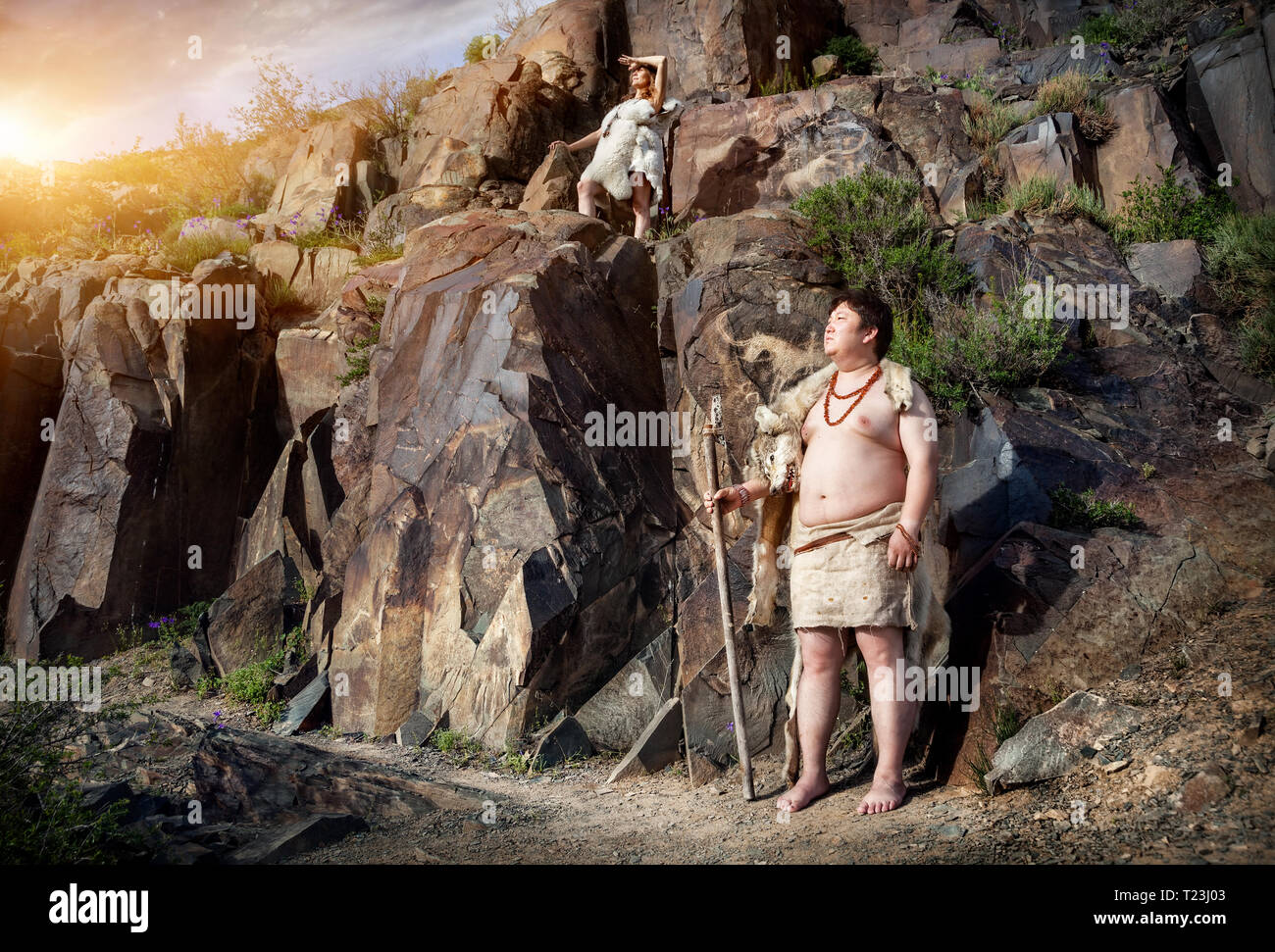 Primitive people dressed in animal skin near ancient cave drawing in the mountains Stock Photo