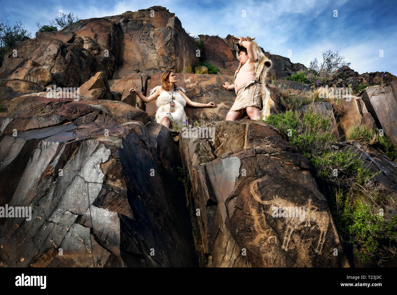 Cave people dressed in animal skin near ancient cave drawing in the rocks Stock Photo