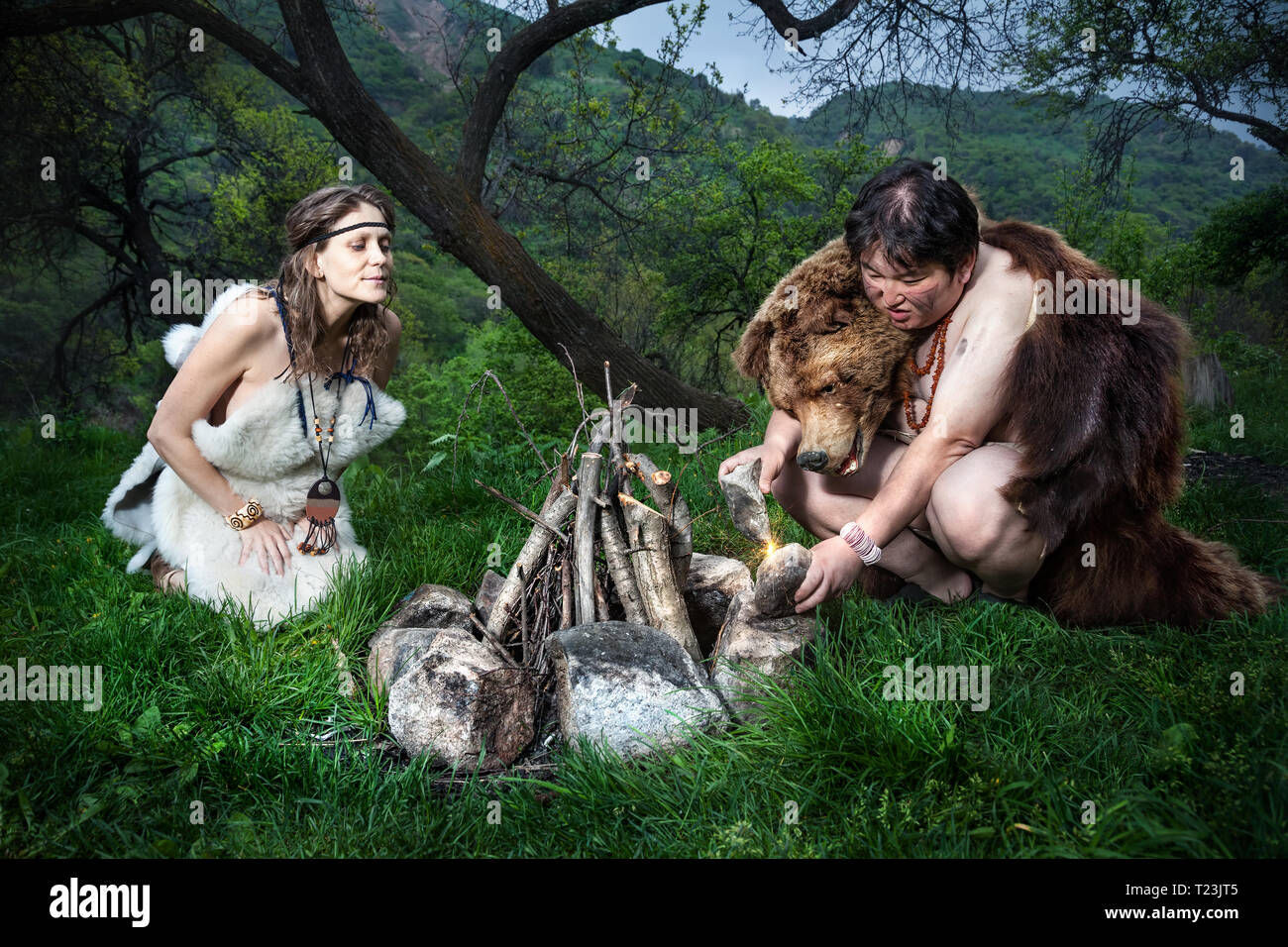 Cave people dressed in animal skin making fire in the forest Stock Photo