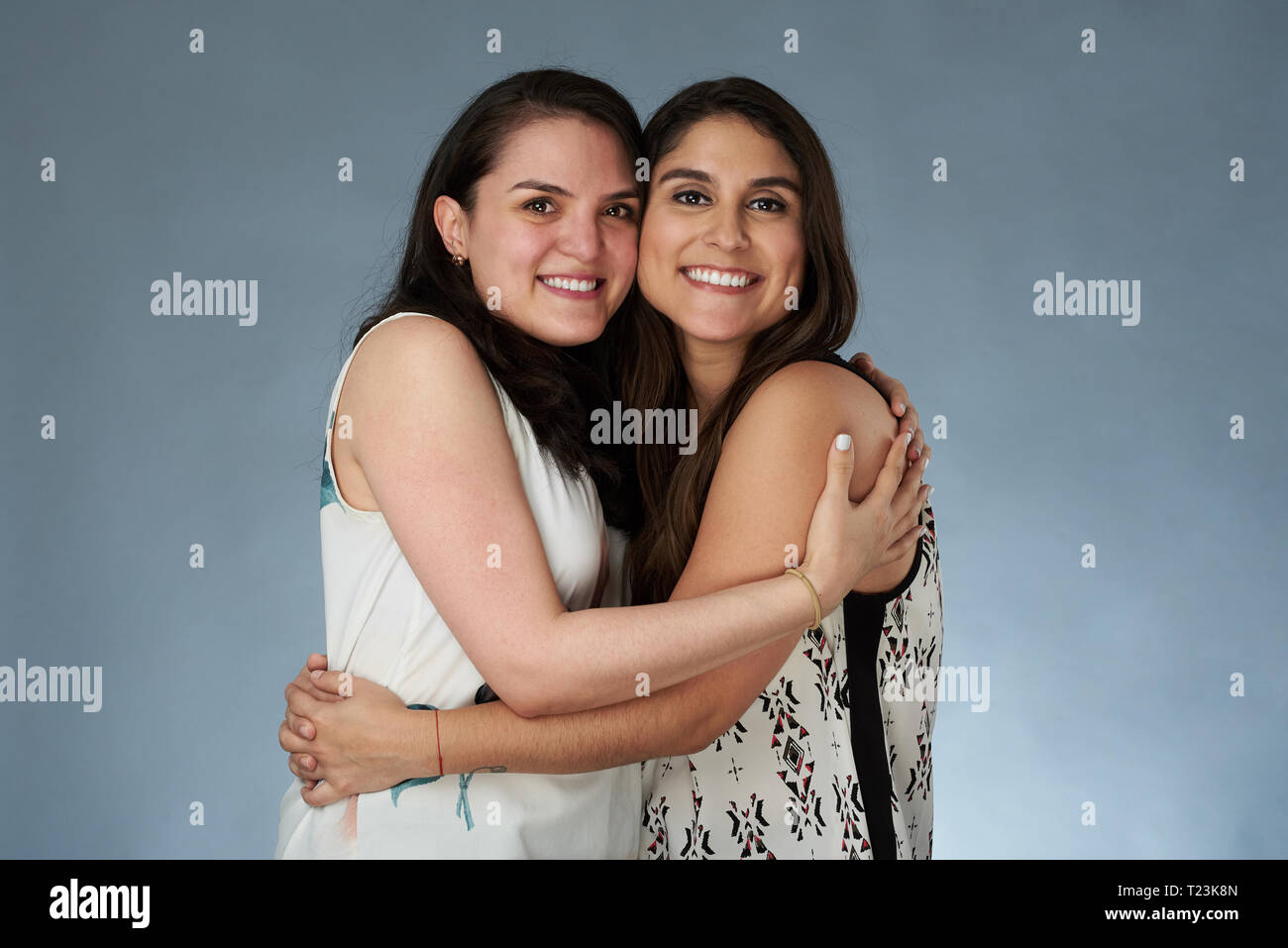 Two brunette friends girls hug on gray studio background Stock Photo