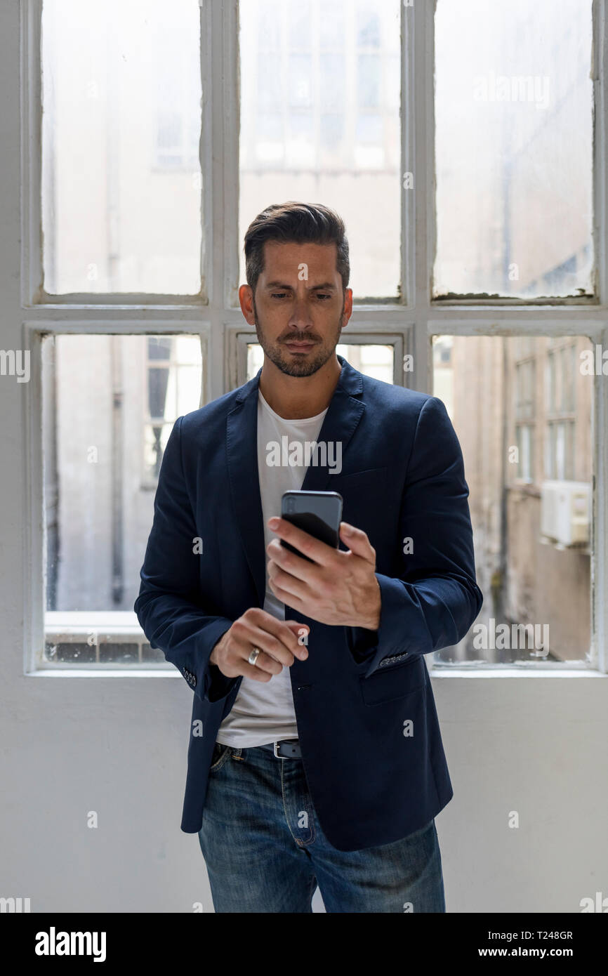 Businessman standing in a loft at the window using cell phone Stock Photo
