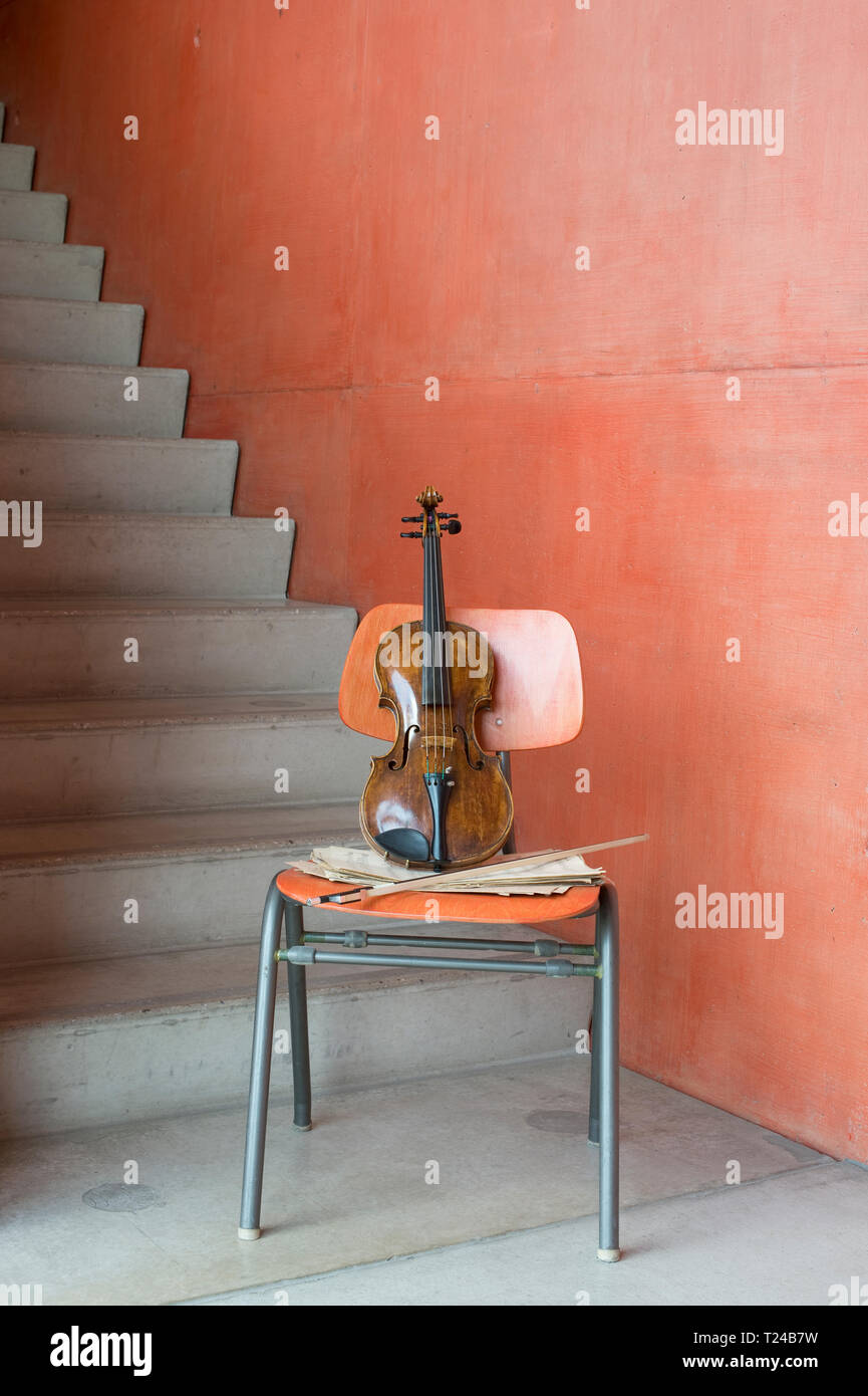 Violin, bow and sheet music on wooden chair at staircase Stock Photo