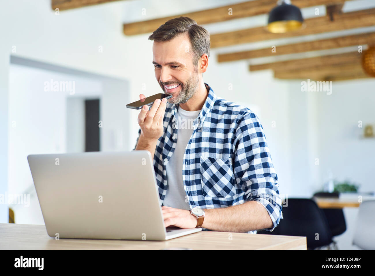 Man talking on phone while working with laptop at home Stock Photo