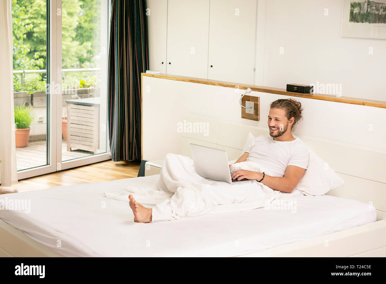 Young man lying on bed, using laptop in the morning Stock Photo