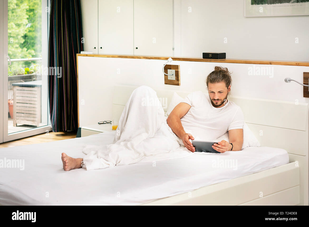 Young man lying on bed, using digital tablet in the morning Stock Photo