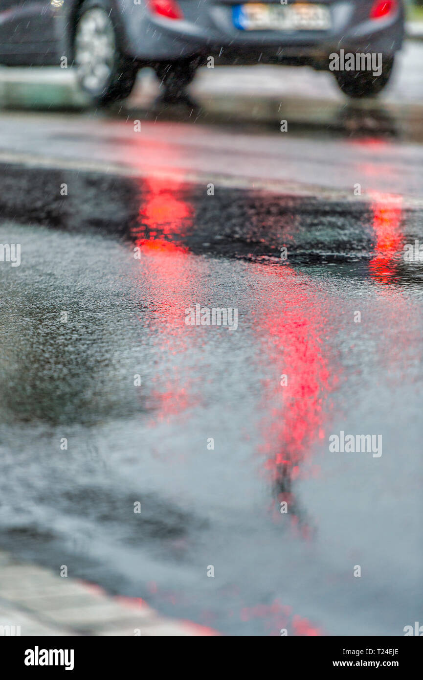 Germany, mirrored red light of traffic light on rain-wet road, rear lights of car Stock Photo