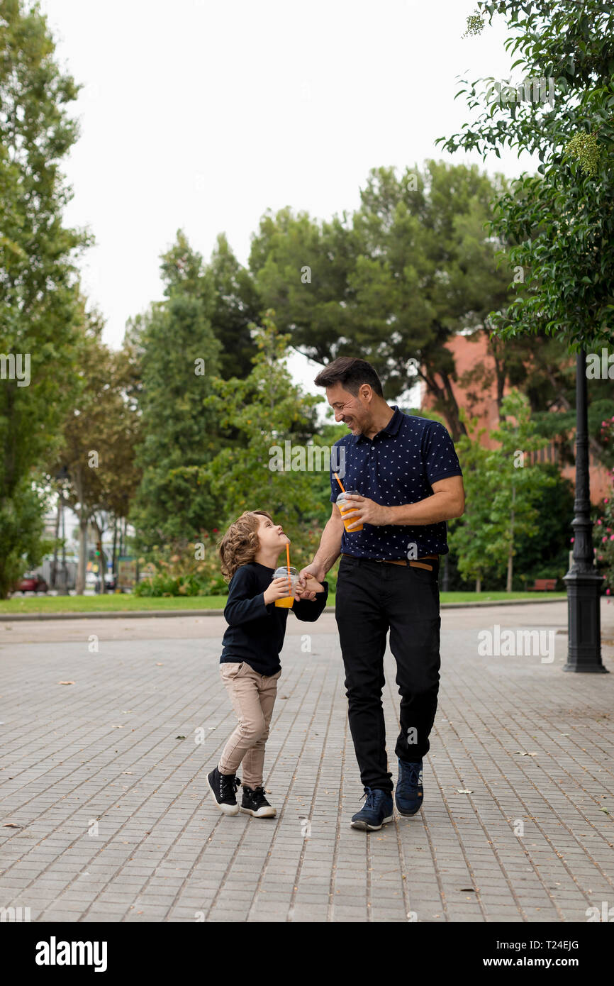 Happy father and son walking hand in hand with soft drinks Stock Photo ...
