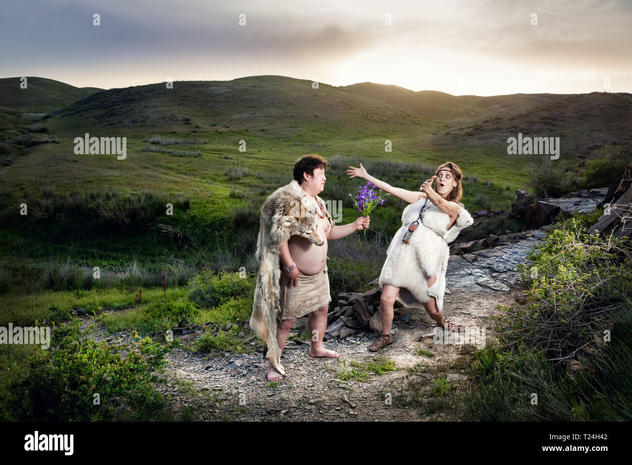 Primitive caveman dressed in animal skin giving flowers to happy cave woman in the mountains Stock Photo