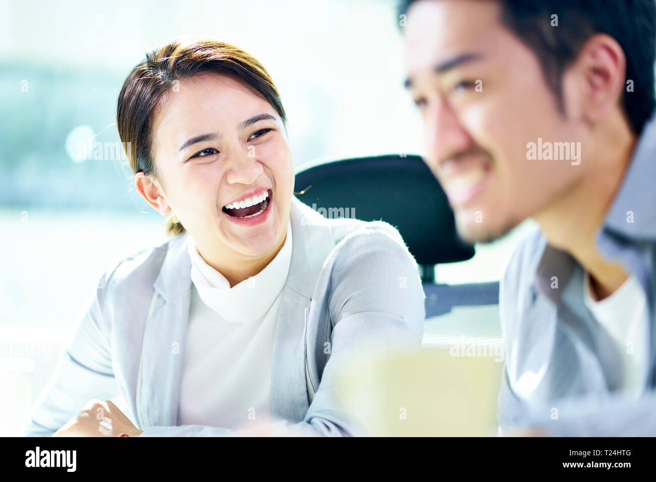 asian businesswoman laughing during meeting with male colleague in office. Stock Photo