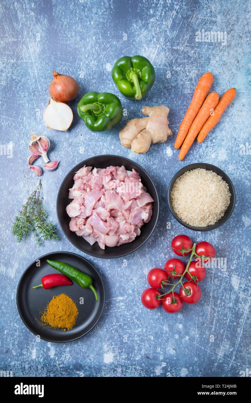 top-view-of-raw-chicken-and-rice-in-dark-bowls-with-root-vegetables-on