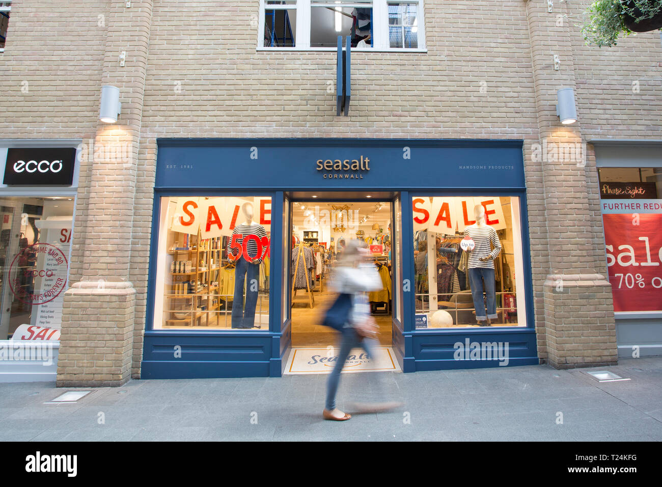 Female shopper walking past sale windows of Seasalt clothing store