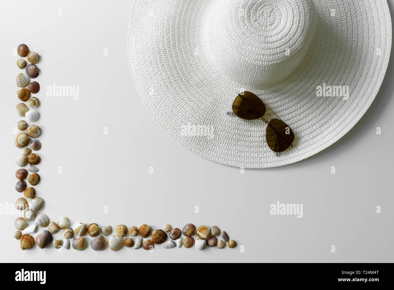 White sun hat decorated with aviator sunglasses accompanied by seashells frame creating summer vibes arrangement. Stock Photo