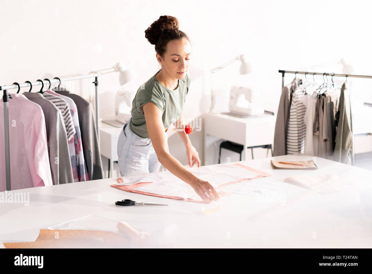 Young attractive woman in casualwear standing by table while taking