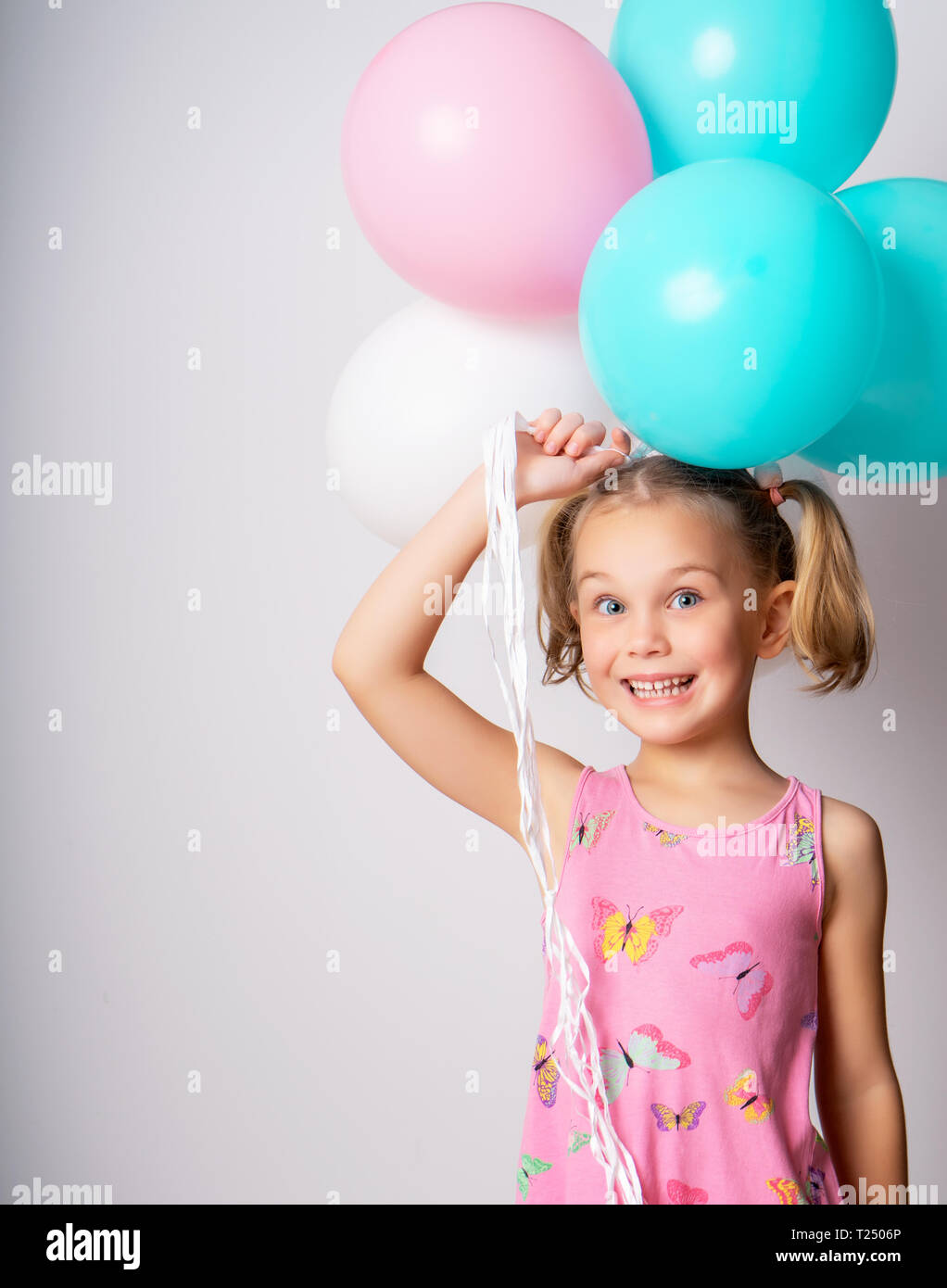 Little cute smiling 5 year old girl holding a bunch of colorful balloons. Stock Photo