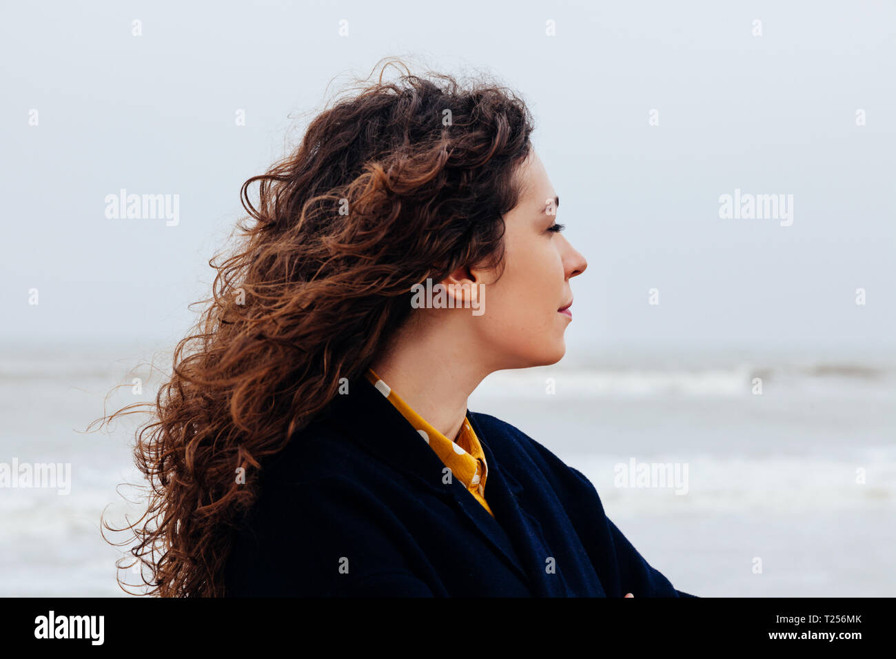 Close-up of a girl with long curly hair against a cold winter sea ...