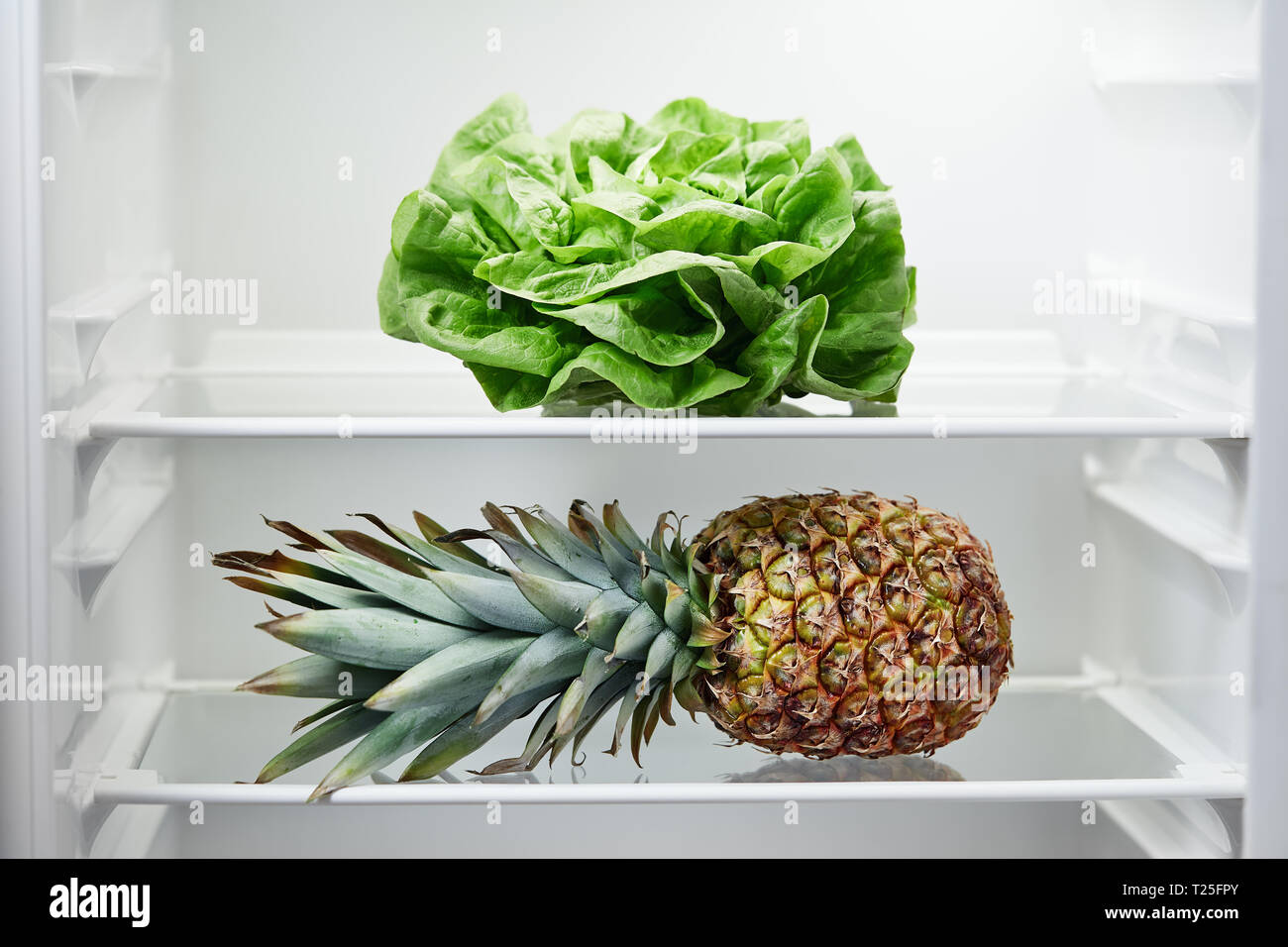 Lettuce and pineapple on shelf in refrigerator. Fridge with open door, close up. Stock Photo
