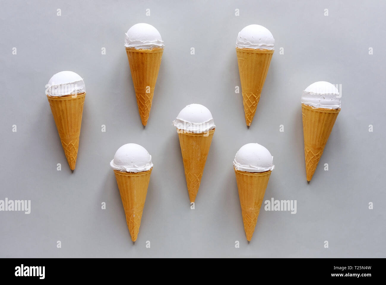 Seven with vanilla ice cream on grey arranged symmetrically around a center cone in a