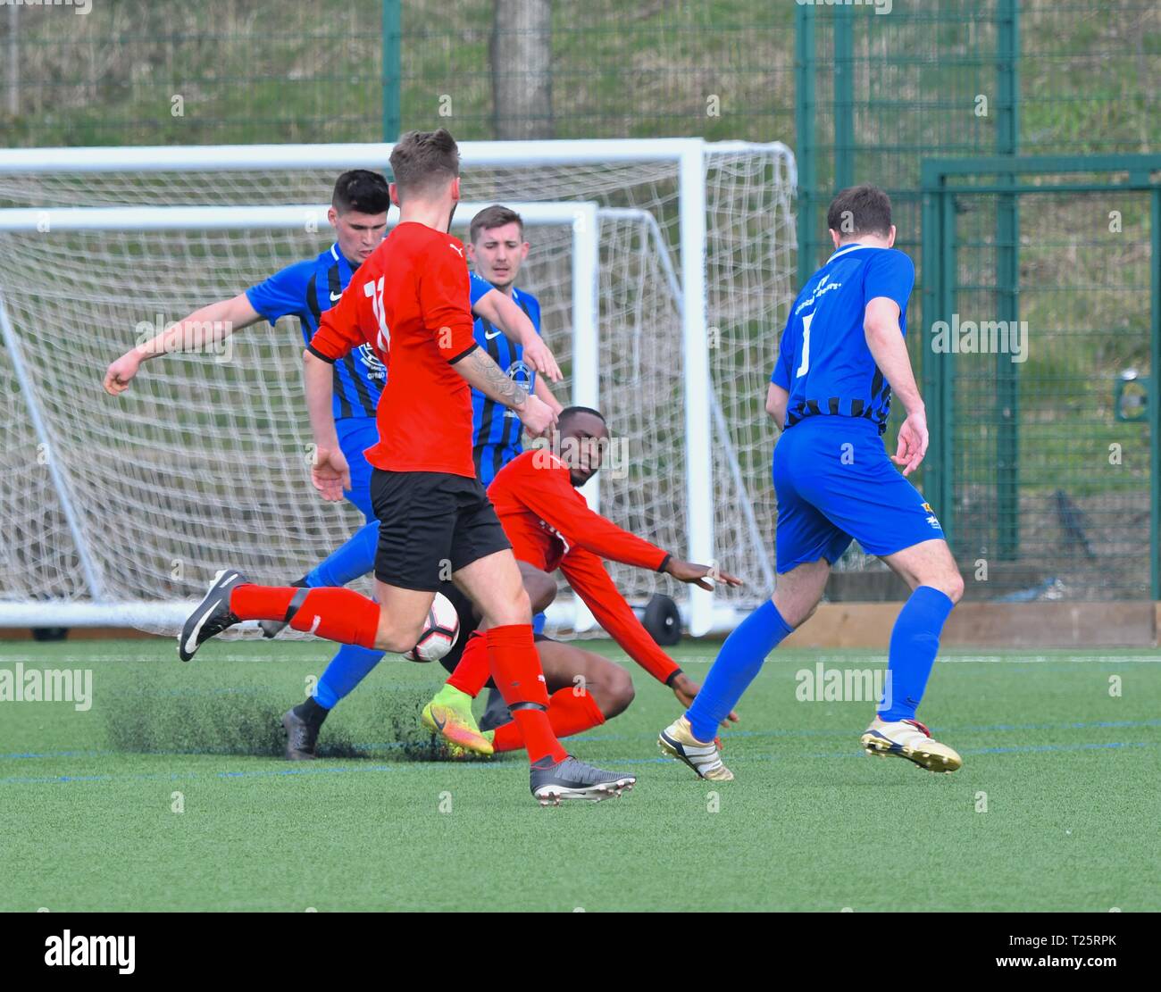 Football action in the  amateur match between Tintwistle Athletic (in blue) and Wilmslow Albion (in red). Stock Photo