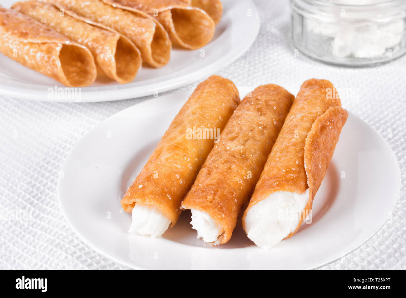 Closeup of cream filled brandy snaps, unfilled snaps, and a pot with cream Stock Photo