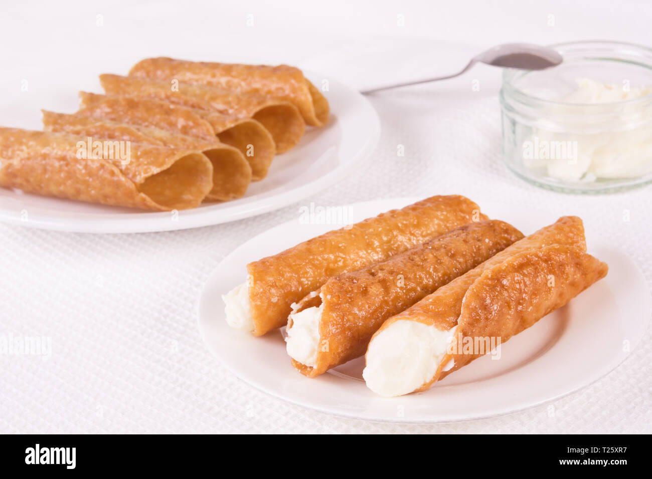Cream filled brandy snaps and unfilled snaps and a pot with cream Stock Photo